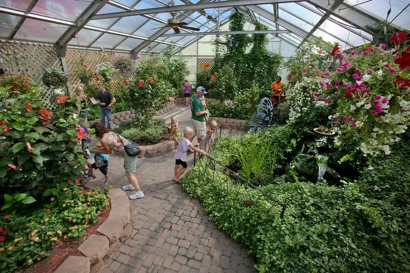 Families walk the brick path through the glass-roofed garden, between raised beds of flowers and vines.